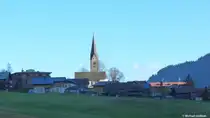 Die katholische Pfarrkirche St. Jodok in Mittelberg, Kleinwalsertal, und das Dach eines der H�user in der N�he werden bereits von der Sonne angeleuchtet; die restlichen H�user liegen am Morgen noch im Schatten (Bezirk Bregenz, Land Voralberg/�sterreich, Oktober 2013).