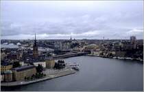 Stockholm vom Turm des Stadshuset aus gesehen: Im Vordergrund der Riddarfj�rden, links Riddarholmen, dahinter Gamla Stan, die Altstadt von Stockholm. Die Br�cken f�hren von dort zum Stadtteil S�dermalm im Hintergrund. Scan vom Dia, 1990 (Matthias)