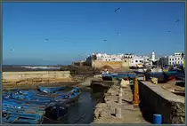 Die Medina von Essaouira liegt direkt an der Atlantikk�ste, gesch�tzt durch die Festungsanlagen Scala de la Kasbah. Die im 18. Jahrhundert errichtete Altstadt mit ihren wei�en H�usern geh�rt seit 2001 zum UNESCO-Weltkulturerbe. Vorn einige der typischen blauen Fischerboote. (Essaouira, 21.11.2015)