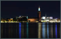 Das zwischen 1911 und 1923 erbaute Rathaus von Stockholm (Stockholms stadshus) liegt auf der Insel Kungsholmen. Am 26.09.2021 spiegeln sich die Lichter des Stadtzentrums im Wasser.