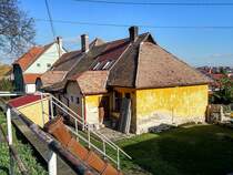 Dieses Foto habe ich in Pcs, in der Stadtteil  Erzsbettelep  (Elisabethsiedlung) gemacht. Dieser Stadteil wurde durch die Donaudampfschiffgesellschaft gegrndet. Die  Kolonie  stand aus 4 Strassen und 32 Huser. Es gab 6 kleine Wohnungen pro Haus zzgl Gartenteil und Nebengebude. Vor ca. 100-120 Jahren wurden neue Kohlenminien in der Nhe erffnet und die dort arbeitenden haben hier Wohnungen bekommen. Die Siedlung hie ursprnglich Ullmannsiedlung, genannt nach einem Leiter des Unternehmens. 1938 wurde auf Elisabethsiedlung umbenannt (von Elisabeth Amalie Eugenie von Wittelsbach Knigin genannt). Die Huser waren berdurchschnittlich ausgerstet, da Leitungswasser und Strom auch vorhanden war. In den vergangenen guten Jahrhundert wurde es nicht geregelt wie man die Gebuden/Wohnungen ndern, erweitern, umbauen oder zusammenlegen/vereinigen darf. Deswegen ist auf heutzutage das Strassenbild ganz ganz gemischt (und daher meiner Meinung nach, sehr einzigartig und interessant) geworden. Die Etagen wurden gendert, Dachgeschosse wurden eingebaut...daher findet man hier keine zwei gleiche Huser. Die groe nderungen sind um ca 1926 begonnen. Wegen der damaligen Wohnungsmangel hat die Stadt 2/3-tel der Siedlung in Miete genommen und hat unter anderem eine Kirche und Schule erbaut und geffnet. Aufnahmezeit: November 2020.
Der Gebudeteil vorne ist vermutlich durch ltere Leute bewohnt die kein Geld und/oder keine Nerven fr eine Sanierung haben.
Hier gilt es auch: 1 Dachfliesentyp = 1 Hausteil = 1 Eigentmer