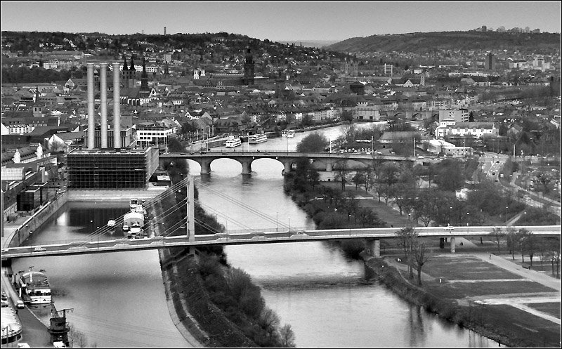 Wrzburg vom Hhenzug im Norden der Stadt aus gesehen. Vorne die neue Brcke der Deutschen Einheit, dahinter die Friedensbrcke, auerdem ist auch noch die Alte Mainbrcke zu erkennen. Links das markante Heizkraftwerk. Dahinter die Altstadt. Rechts oben auf dem Berg sind die Hochhuser von der Trabantenstadt Heuchelhof zu erkennen. 15.4.2006 (Matthias)